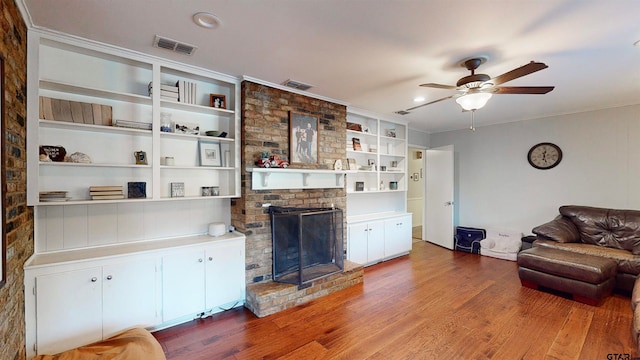 living room with hardwood / wood-style floors, ceiling fan, crown molding, and a brick fireplace