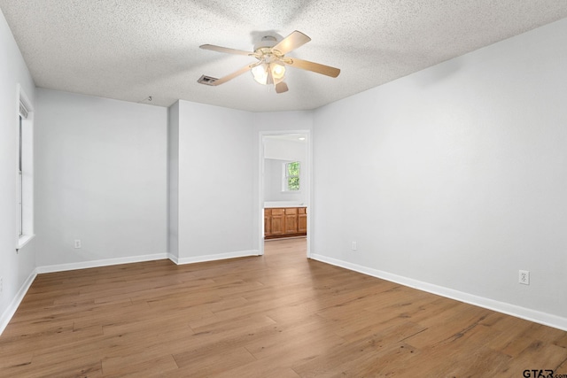 empty room featuring light wood-style floors, a textured ceiling, a ceiling fan, and baseboards