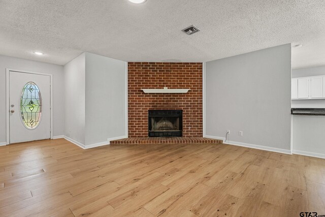 unfurnished living room with visible vents, baseboards, a fireplace, light wood-style flooring, and a textured ceiling