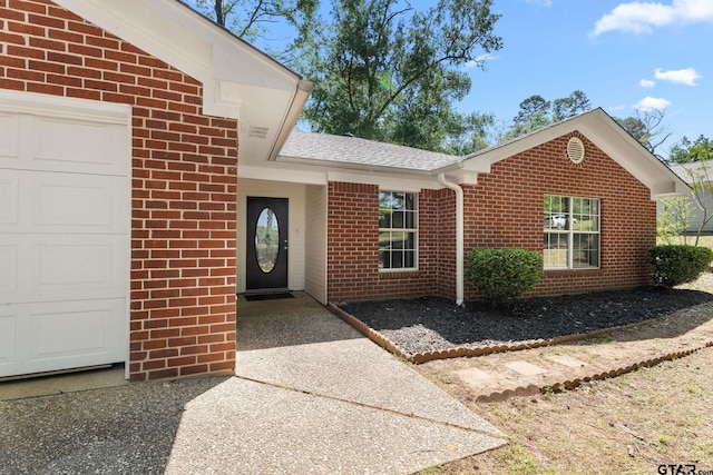 view of exterior entry with brick siding, roof with shingles, and a garage