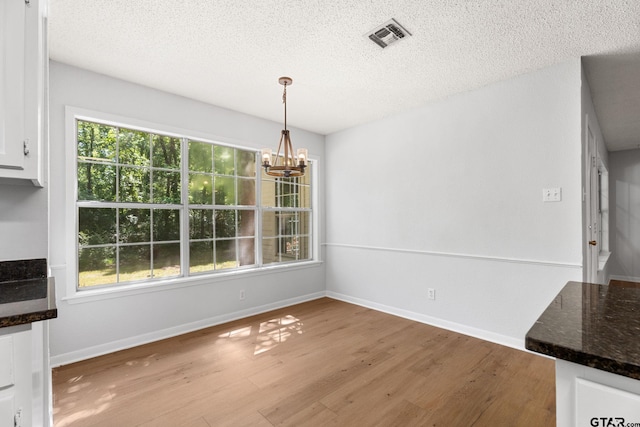 unfurnished dining area featuring visible vents, baseboards, light wood-style flooring, a textured ceiling, and a notable chandelier