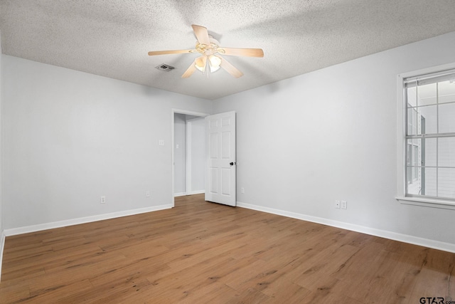 empty room featuring wood finished floors, visible vents, a ceiling fan, baseboards, and a textured ceiling