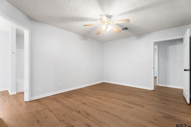 empty room with wood finished floors, visible vents, a textured ceiling, and ceiling fan