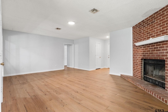 unfurnished living room featuring a brick fireplace, wood finished floors, visible vents, baseboards, and a textured ceiling