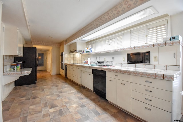 kitchen with backsplash, tile countertops, black appliances, and white cabinetry