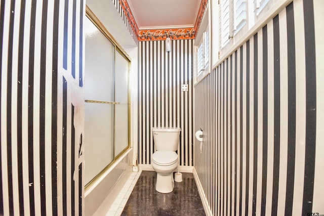 bathroom featuring toilet and shower / bath combination with glass door