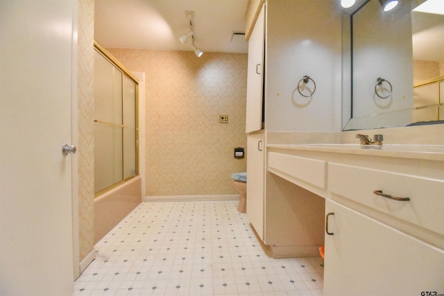 full bathroom with track lighting, bath / shower combo with glass door, vanity, and toilet