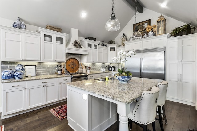 kitchen with sink, hanging light fixtures, a kitchen island with sink, stainless steel appliances, and custom range hood