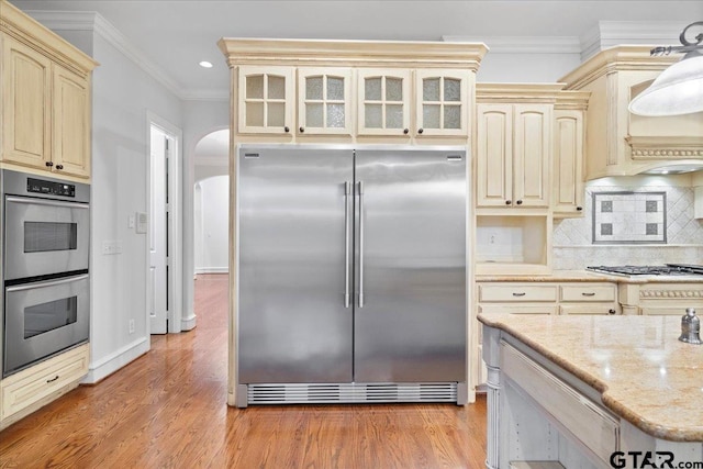 kitchen with light hardwood / wood-style floors, cream cabinets, tasteful backsplash, crown molding, and appliances with stainless steel finishes