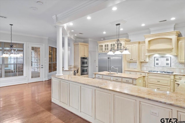 kitchen featuring appliances with stainless steel finishes, pendant lighting, light stone countertops, dark wood-type flooring, and decorative columns