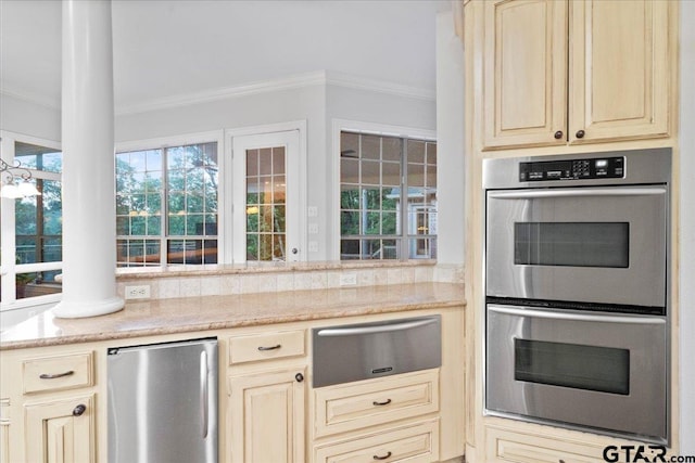 kitchen with decorative columns, cream cabinetry, ornamental molding, and stainless steel appliances