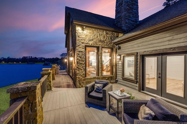 deck at dusk featuring french doors and a water view