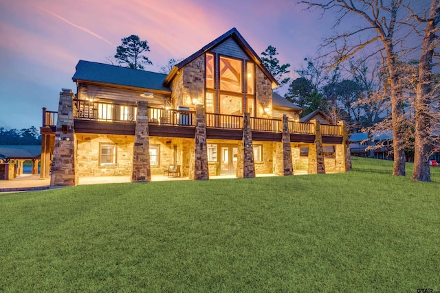 back of house at dusk featuring stone siding and a lawn