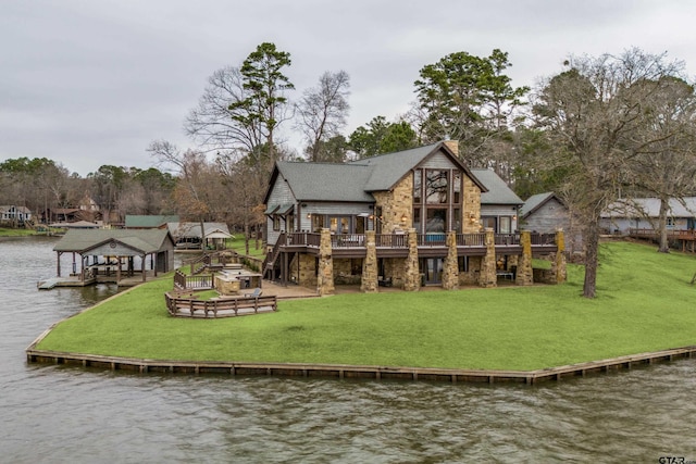 rear view of house with a deck with water view, stone siding, a lawn, and roof with shingles