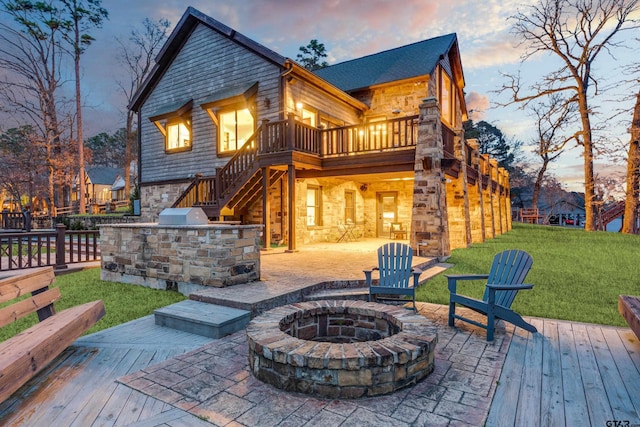 back of property at dusk featuring a fire pit, a lawn, a deck, a patio area, and stone siding