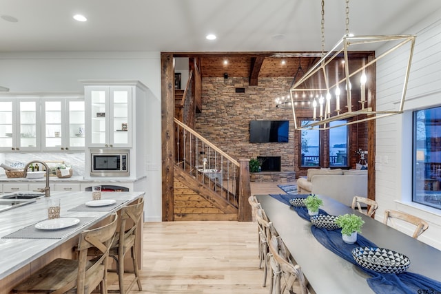 dining area with light wood-type flooring, beam ceiling, a notable chandelier, a fireplace, and stairs