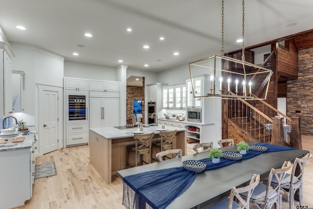 kitchen with a kitchen island with sink, recessed lighting, light wood-style floors, white cabinets, and built in appliances