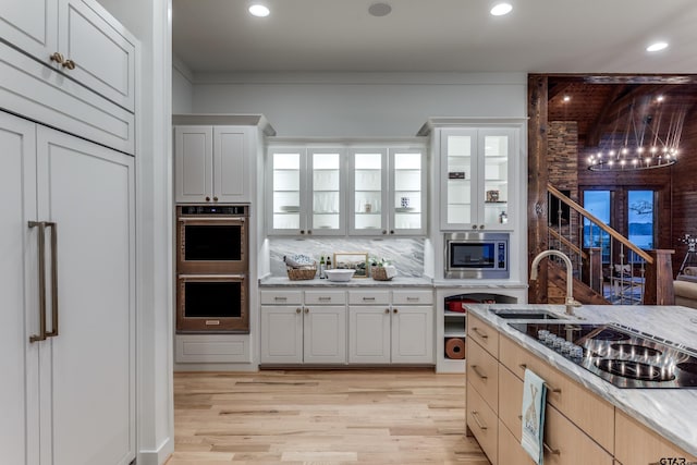 kitchen featuring light stone counters, light wood finished floors, a sink, decorative backsplash, and appliances with stainless steel finishes