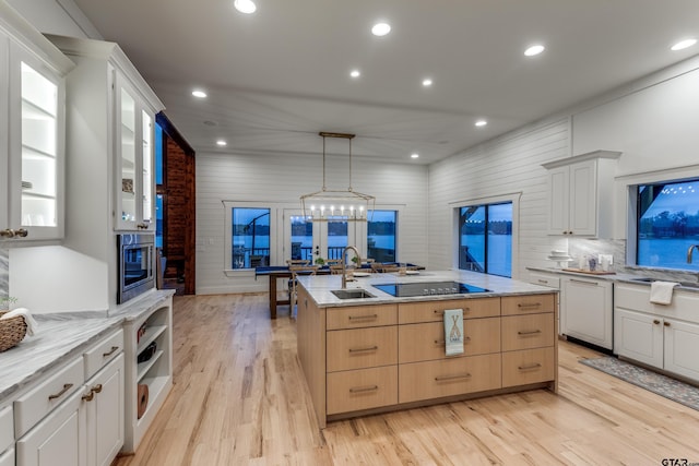 kitchen with light wood finished floors, recessed lighting, a kitchen island with sink, a sink, and black electric stovetop