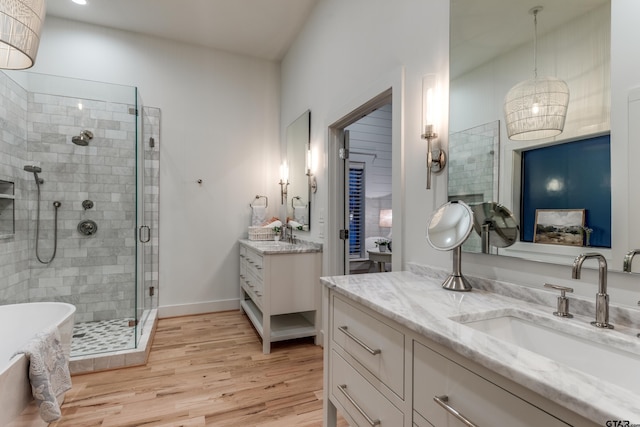 bathroom with wood finished floors, a shower stall, baseboards, a soaking tub, and vanity