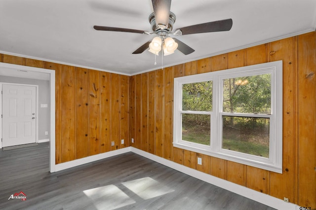 unfurnished room featuring ornamental molding, dark hardwood / wood-style flooring, wood walls, and ceiling fan