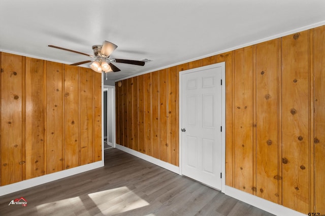 unfurnished room featuring ornamental molding, dark hardwood / wood-style flooring, wooden walls, and ceiling fan