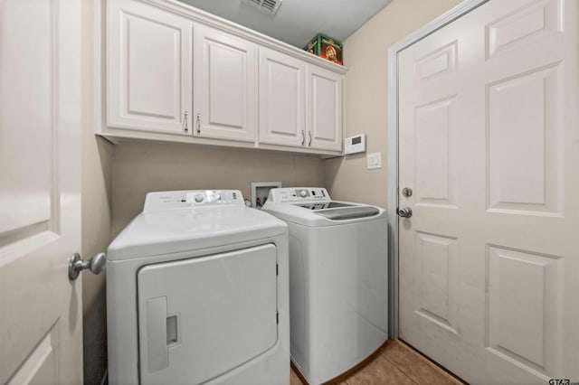 clothes washing area featuring cabinets, light tile patterned floors, and washing machine and clothes dryer