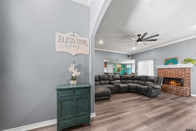 living room with hardwood / wood-style floors, a brick fireplace, ceiling fan, and ornamental molding