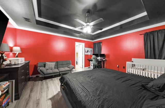 bedroom featuring hardwood / wood-style flooring, ceiling fan, ornamental molding, and a tray ceiling