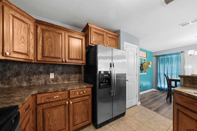 kitchen with decorative backsplash, stainless steel refrigerator with ice dispenser, dark stone countertops, a chandelier, and light hardwood / wood-style floors