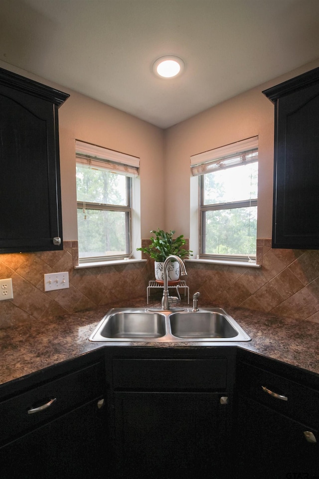 kitchen with a sink, dark cabinets, backsplash, and dark countertops