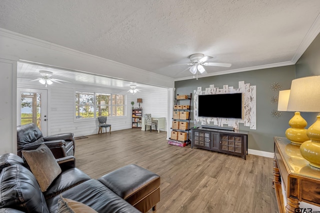 living room featuring ceiling fan, ornamental molding, a textured ceiling, and light wood-type flooring