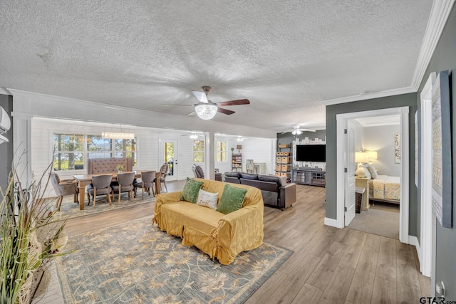 living room featuring ceiling fan, light hardwood / wood-style flooring, ornamental molding, and a textured ceiling