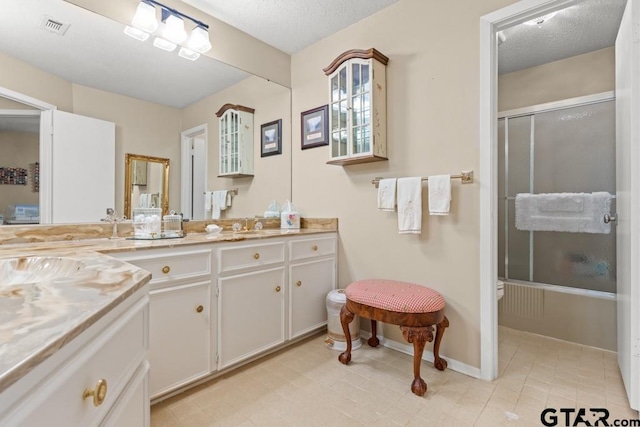 bathroom with shower / bath combination with glass door, vanity, and a textured ceiling