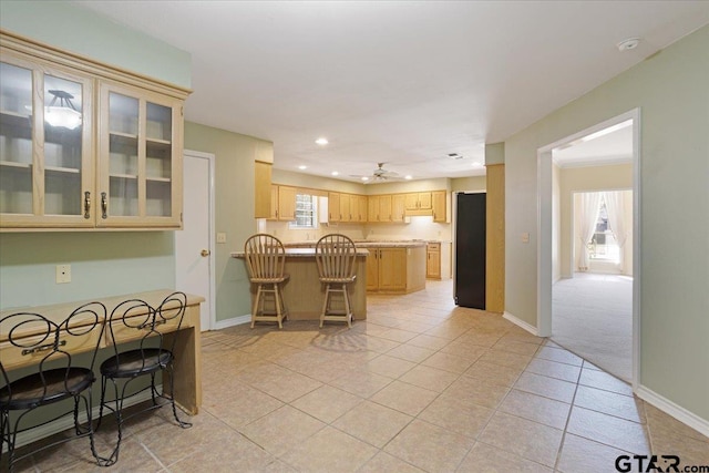 kitchen featuring ceiling fan, a center island, black refrigerator, a breakfast bar, and light tile patterned floors