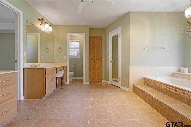 bathroom featuring ceiling fan, tile patterned flooring, a relaxing tiled tub, toilet, and vanity