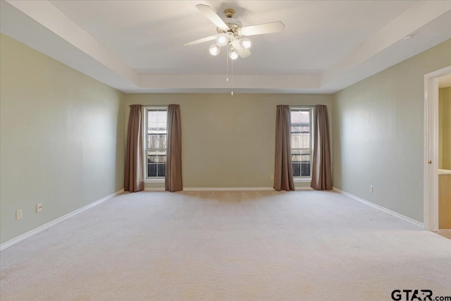 carpeted spare room with a tray ceiling, ceiling fan, and a healthy amount of sunlight