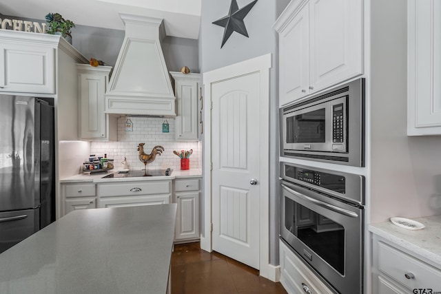 kitchen featuring premium range hood, white cabinetry, appliances with stainless steel finishes, light stone countertops, and decorative backsplash