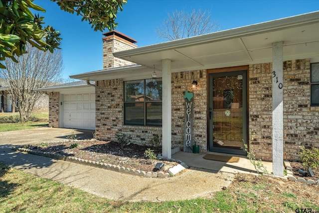 doorway to property featuring a garage, brick siding, driveway, and a chimney