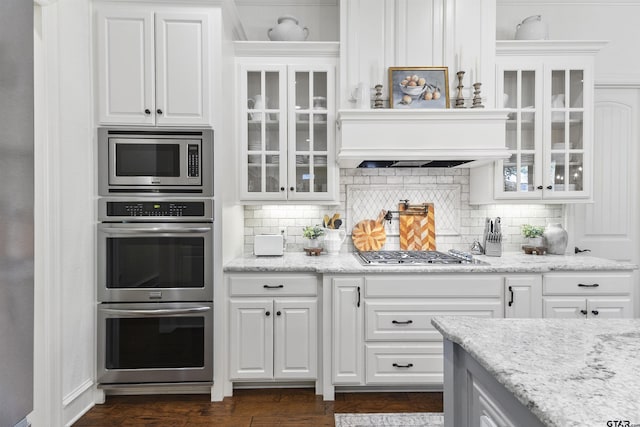 kitchen featuring custom range hood, stainless steel appliances, white cabinetry, and tasteful backsplash