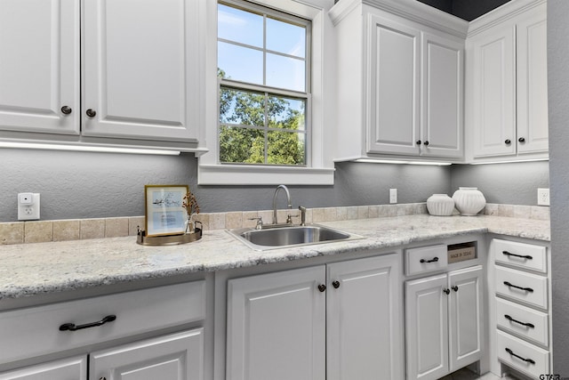 kitchen with light stone counters, white cabinetry, and sink