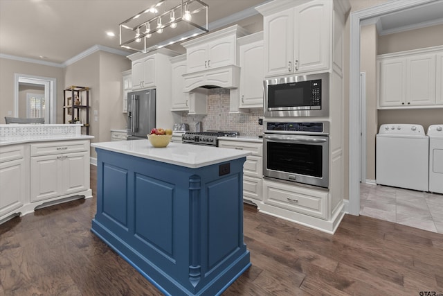 kitchen with washer and clothes dryer, a center island, white cabinets, decorative light fixtures, and stainless steel appliances