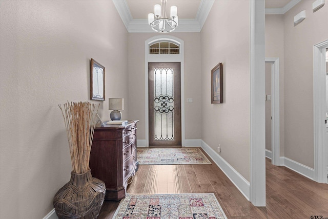 foyer entrance with wood-type flooring, ornamental molding, and a notable chandelier