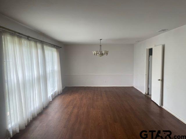 spare room featuring baseboards, an inviting chandelier, and wood finished floors