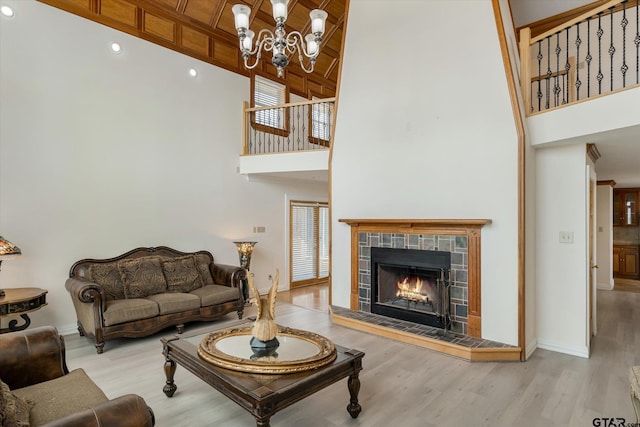 living room with a fireplace, a chandelier, a high ceiling, and light wood-type flooring