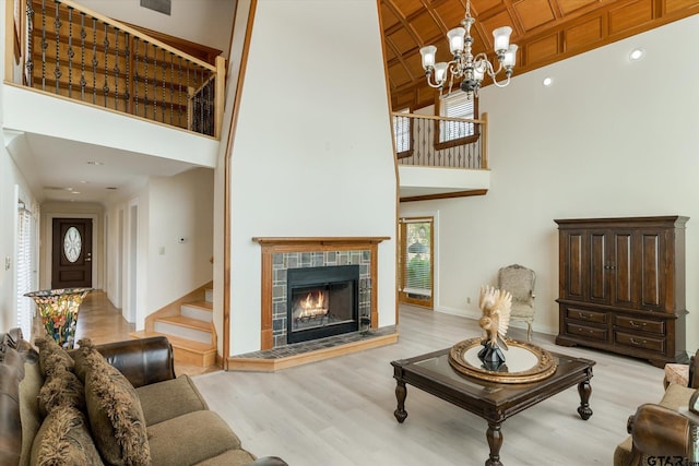 living room with a towering ceiling, a tiled fireplace, a notable chandelier, and light wood-type flooring