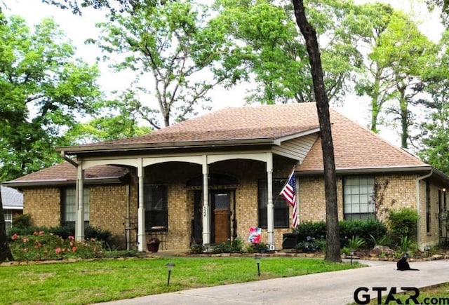 view of front of home featuring roof with shingles, brick siding, and a front lawn