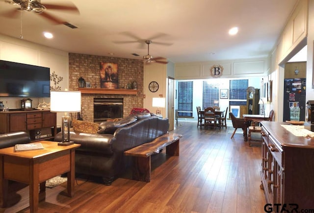 living area with a fireplace, a ceiling fan, visible vents, and dark wood-style floors