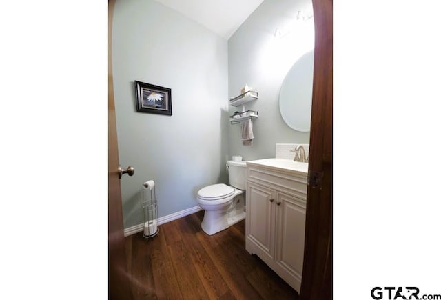 half bath featuring toilet, wood finished floors, vanity, vaulted ceiling, and baseboards