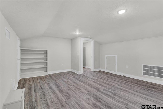 additional living space with light wood-type flooring, a textured ceiling, and vaulted ceiling